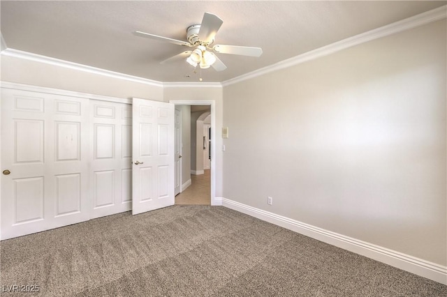 unfurnished bedroom with carpet floors, ornamental molding, a closet, baseboards, and a ceiling fan