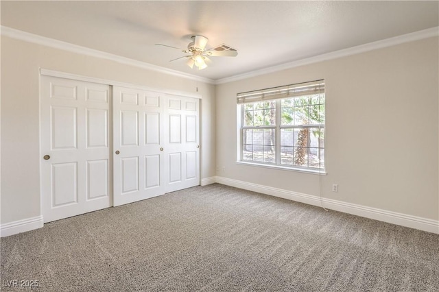 unfurnished bedroom with crown molding, carpet flooring, ceiling fan, baseboards, and a closet