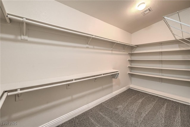 walk in closet with visible vents, dark carpet, and vaulted ceiling