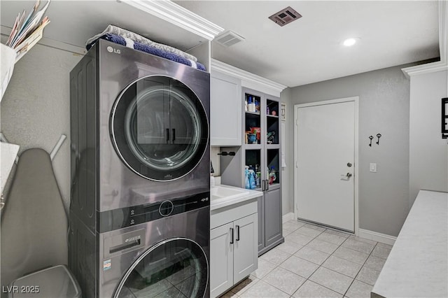 laundry room featuring light tile patterned floors, cabinet space, stacked washer / dryer, and visible vents