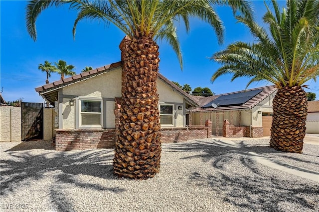 view of front of home featuring a gate, roof mounted solar panels, stucco siding, and fence