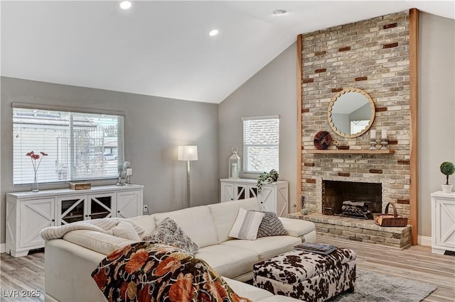 living area featuring baseboards, light wood finished floors, a brick fireplace, and lofted ceiling