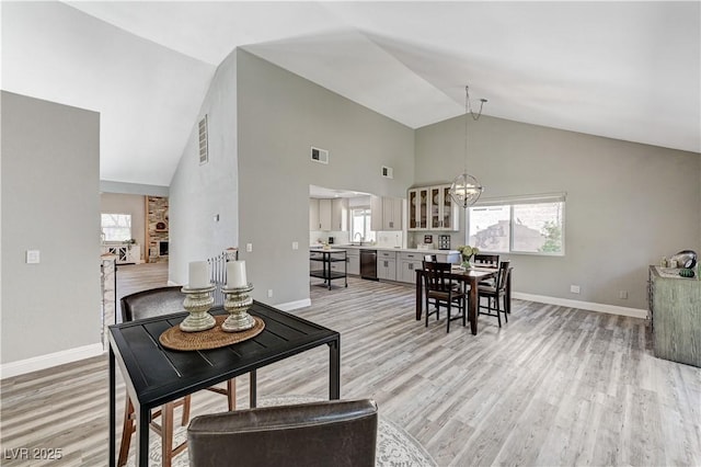 dining space with visible vents, light wood finished floors, baseboards, and high vaulted ceiling