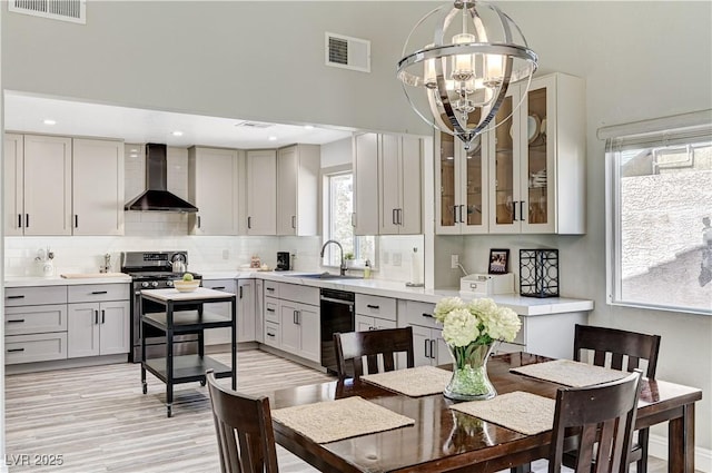 kitchen featuring wall chimney range hood, stainless steel gas range, a sink, and visible vents