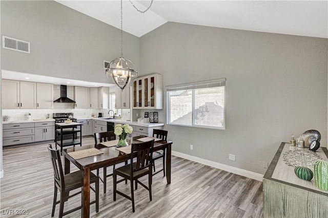 dining room with light wood-style floors, high vaulted ceiling, a chandelier, baseboards, and visible vents