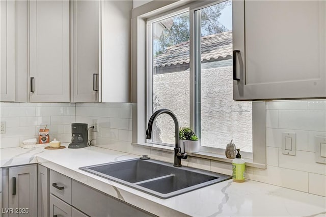 kitchen featuring light stone countertops, gray cabinetry, a sink, and tasteful backsplash