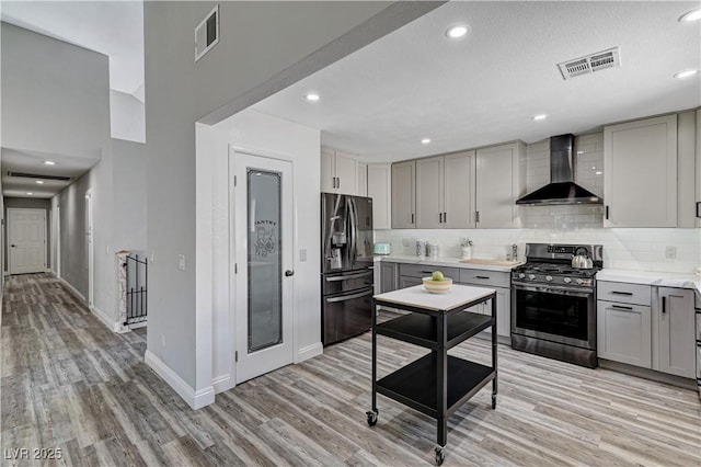 kitchen with gas stove, wall chimney range hood, light wood finished floors, black fridge, and gray cabinetry