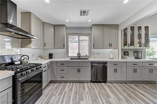 kitchen with wall chimney range hood, a sink, visible vents, stainless steel appliances, and gray cabinetry