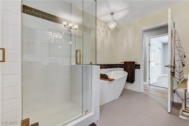 full bath featuring toilet, tile patterned floors, a freestanding bath, a shower stall, and a notable chandelier