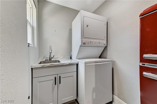 laundry room featuring stacked washer / drying machine, a textured wall, and a sink