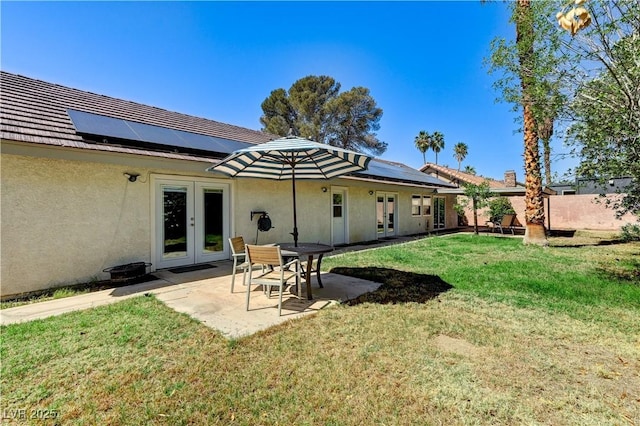 rear view of property featuring a yard, french doors, solar panels, and stucco siding