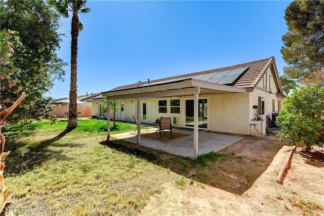 back of house featuring solar panels, a patio area, fence, a yard, and stucco siding