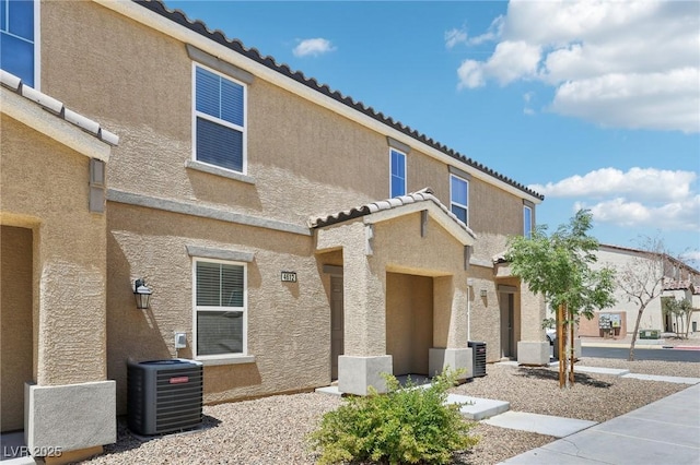 exterior space with a tiled roof, central AC, and stucco siding