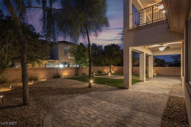 patio terrace at dusk featuring a fenced backyard and a balcony