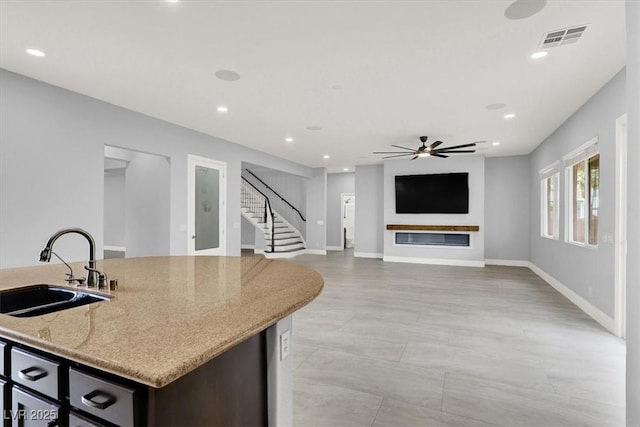 kitchen with ceiling fan, light stone countertops, a sink, baseboards, and visible vents