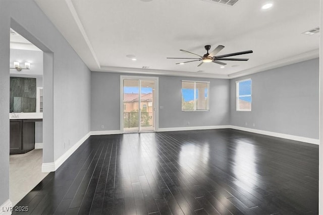 empty room featuring ceiling fan, visible vents, a wealth of natural light, and dark wood finished floors