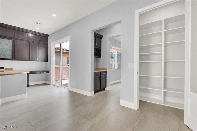 kitchen with built in features, light tile patterned flooring, dark brown cabinets, baseboards, and light countertops