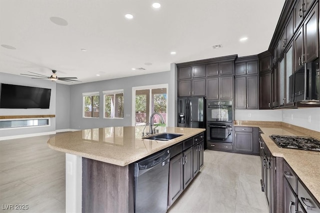 kitchen with a sink, light stone counters, black appliances, recessed lighting, and an island with sink