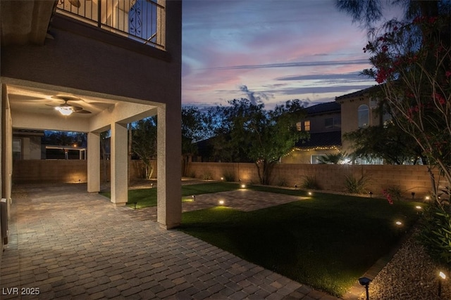 yard at dusk featuring a fenced backyard, ceiling fan, and a patio area
