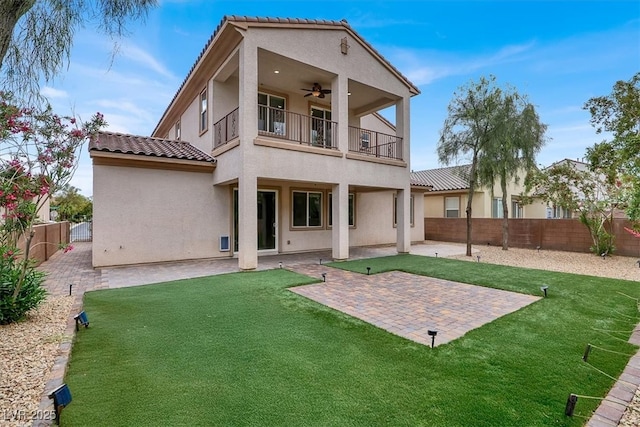 back of house with ceiling fan, stucco siding, a fenced backyard, a balcony, and a yard