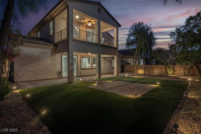 rear view of house featuring a tiled roof, a lawn, a balcony, a fenced backyard, and stucco siding