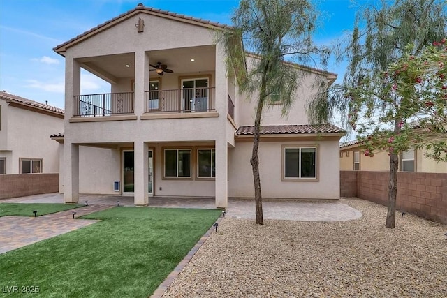 back of house featuring a tiled roof, a fenced backyard, stucco siding, and a balcony