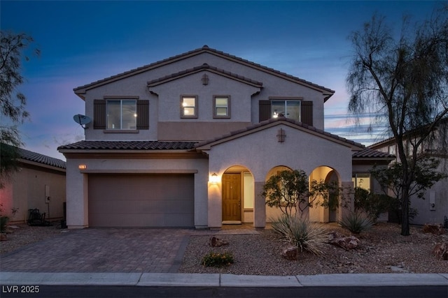 mediterranean / spanish house with stucco siding, an attached garage, decorative driveway, and a tile roof