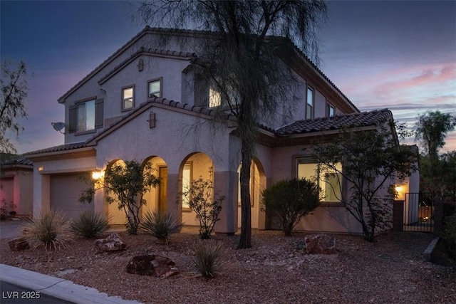 mediterranean / spanish home with a garage, stucco siding, and a tiled roof