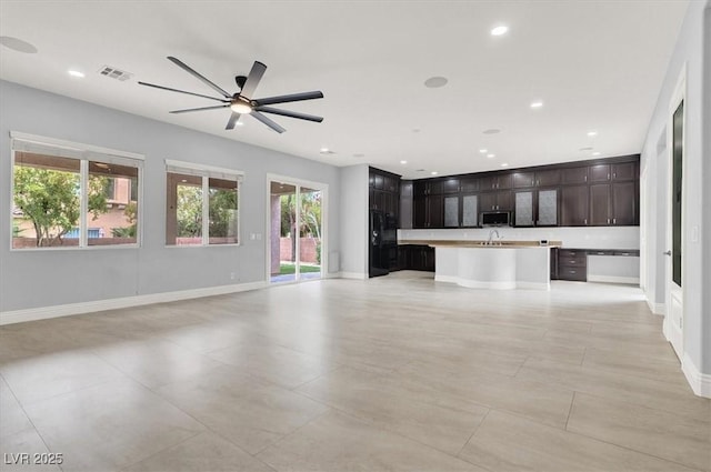unfurnished living room featuring baseboards, plenty of natural light, ceiling fan, and visible vents