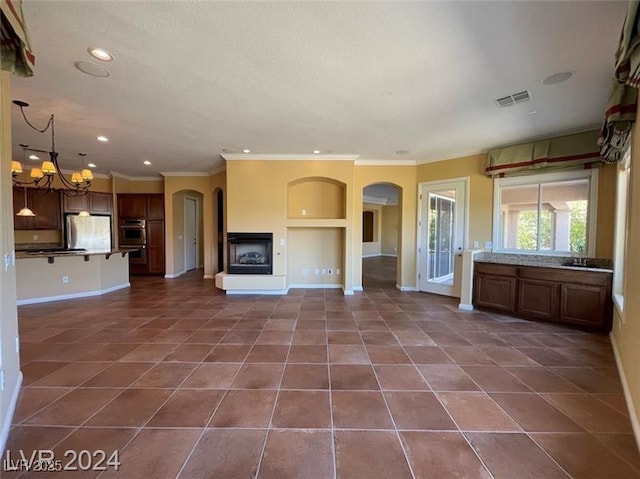 unfurnished living room with visible vents, crown molding, dark tile patterned flooring, and an inviting chandelier