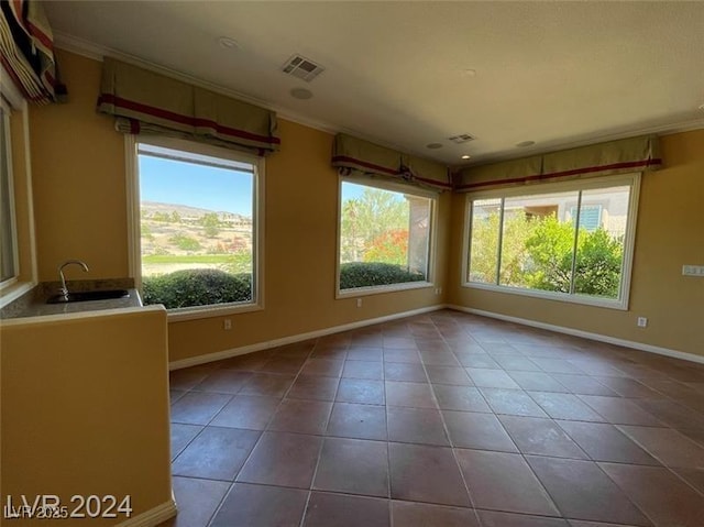 tiled empty room featuring a sink, baseboards, plenty of natural light, and visible vents