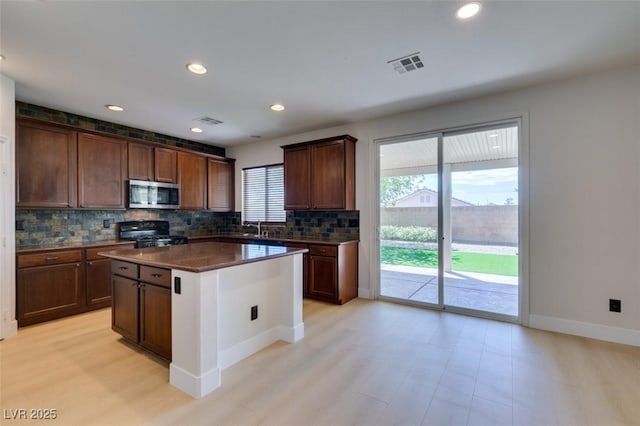 kitchen with dark countertops, stainless steel microwave, decorative backsplash, visible vents, and range with gas cooktop
