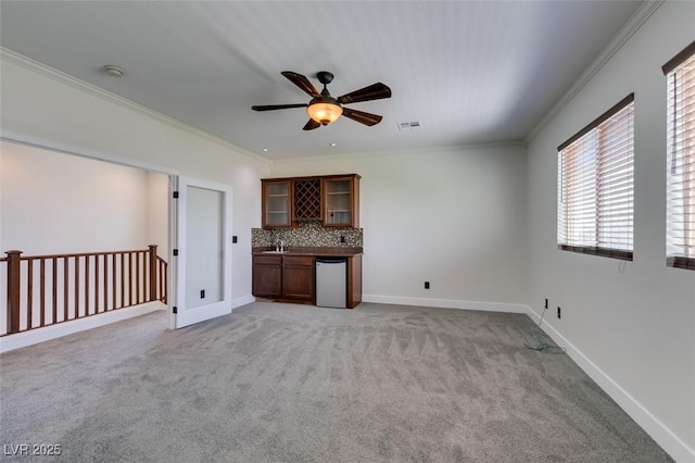 unfurnished living room featuring crown molding, light carpet, a ceiling fan, visible vents, and bar area