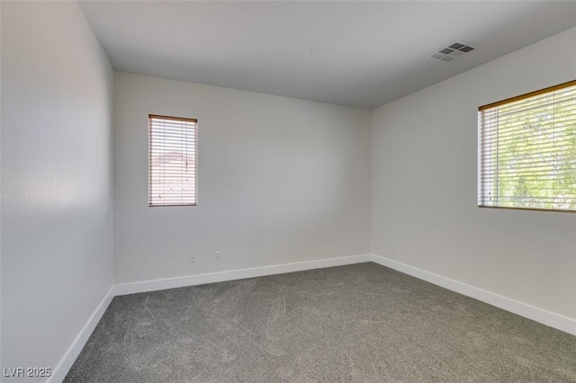 unfurnished room with baseboards, dark colored carpet, and visible vents