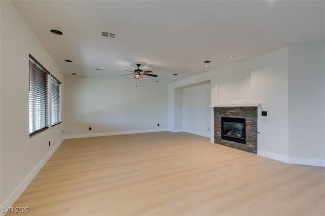 unfurnished living room with a ceiling fan, visible vents, a fireplace, baseboards, and light wood finished floors