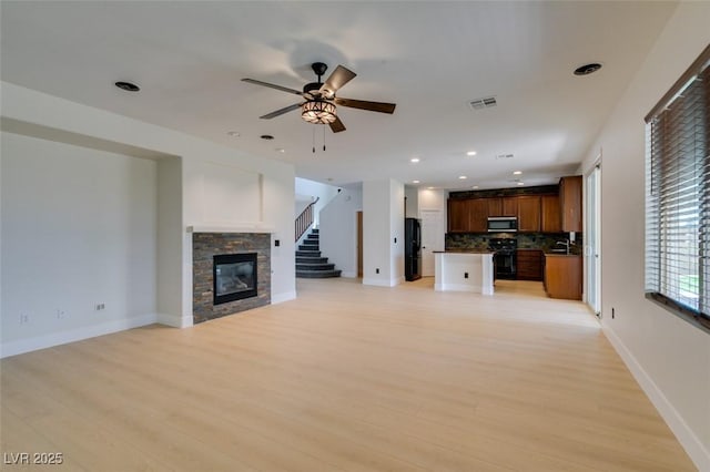 unfurnished living room featuring ceiling fan, visible vents, a fireplace, baseboards, and light wood-style flooring