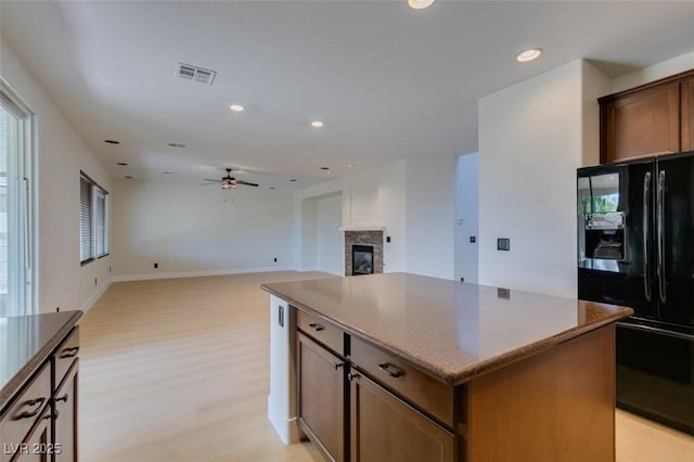 kitchen with ceiling fan, a stone fireplace, visible vents, a center island, and black refrigerator with ice dispenser