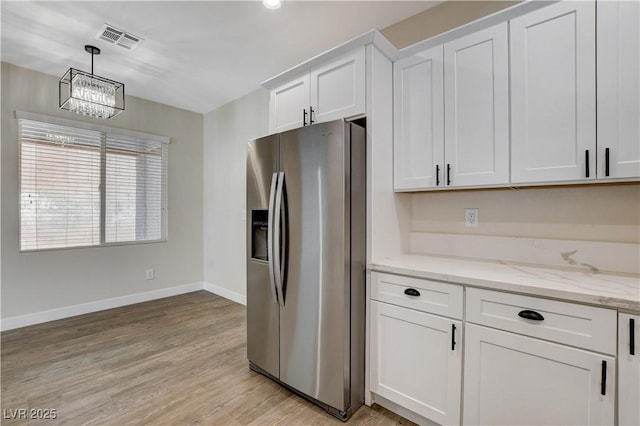 kitchen featuring stainless steel refrigerator with ice dispenser, visible vents, baseboards, white cabinets, and an inviting chandelier