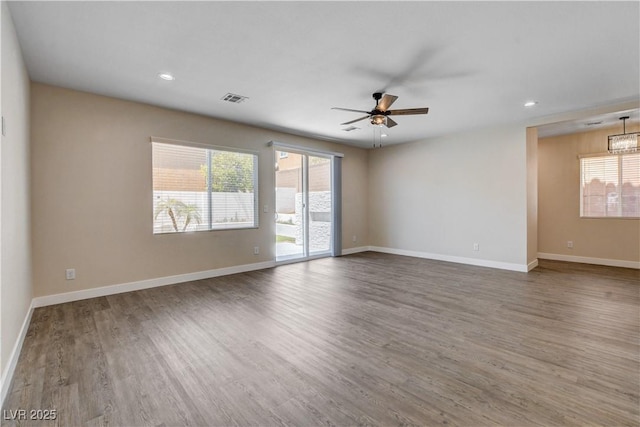 empty room featuring visible vents, a ceiling fan, baseboards, and wood finished floors