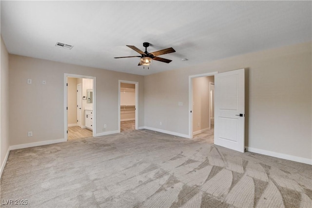 unfurnished bedroom featuring a walk in closet, visible vents, baseboards, a closet, and light carpet