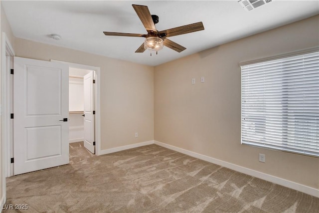 unfurnished bedroom featuring a walk in closet, baseboards, light colored carpet, and visible vents