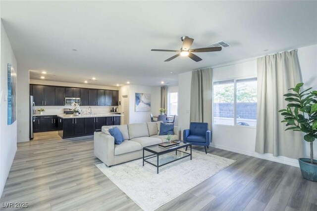 living room with ceiling fan, visible vents, baseboards, light wood finished floors, and recessed lighting