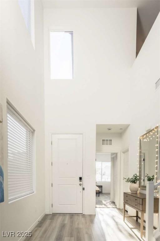 foyer featuring baseboards, visible vents, light wood-style flooring, and a towering ceiling