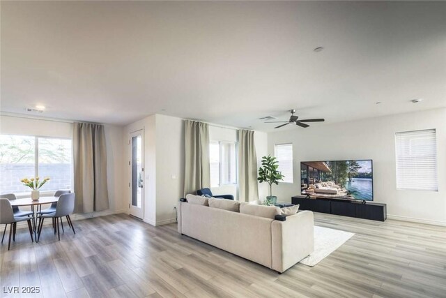 living area featuring light wood-style floors, a ceiling fan, and baseboards
