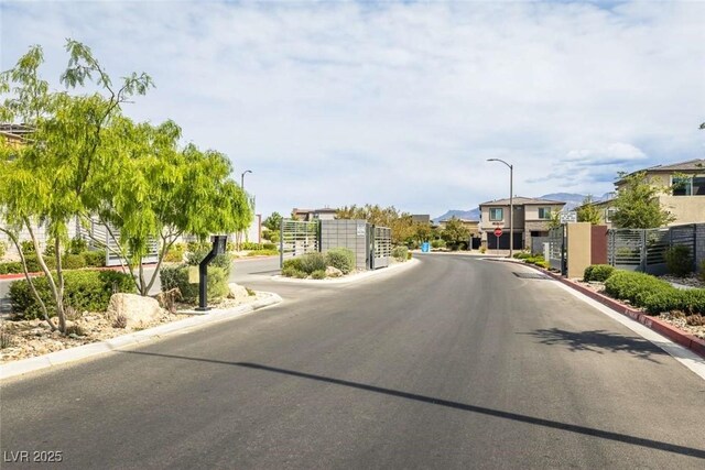view of street featuring street lights, a gated entry, a residential view, and curbs