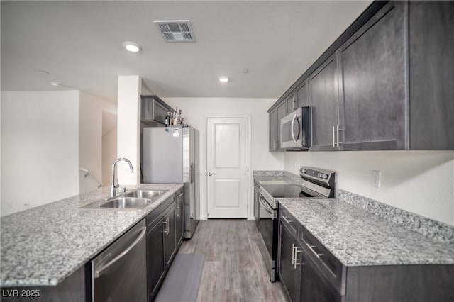 kitchen featuring a sink, stainless steel appliances, a peninsula, wood finished floors, and visible vents