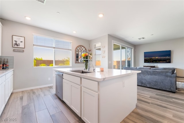 23 Strada Barbera, Henderson, NV 89011 - kitchen with stainless steel dishwasher, a kitchen island with sink, light wood-style flooring, white cabinetry, and light countertops