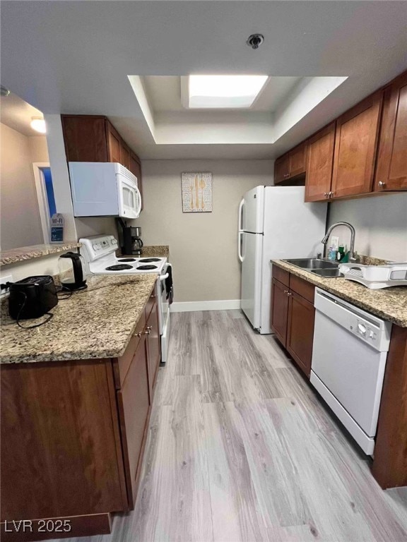 kitchen featuring a sink, white appliances, baseboards, light wood-type flooring, and a tray ceiling