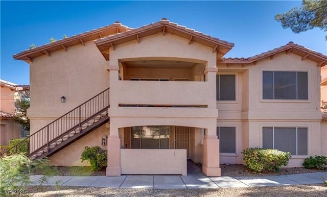 view of front of home with stairs, stucco siding, a tiled roof, and a balcony