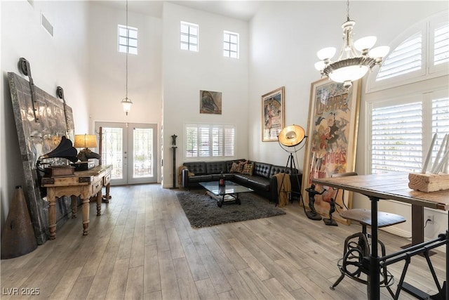 living room with wood finished floors, a wealth of natural light, french doors, and a towering ceiling